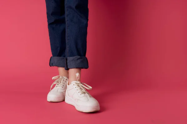Weibliche Füße weiße Turnschuhe Straßenmode rosa Hintergrund — Stockfoto