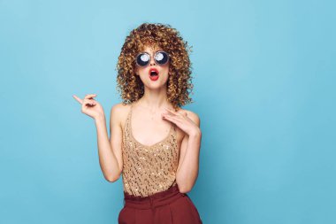 Büyüleyici model kıvırcık saçlar. Şaşırtıcı. Koyu güneş gözlüğü stüdyo mavi arka plan. 