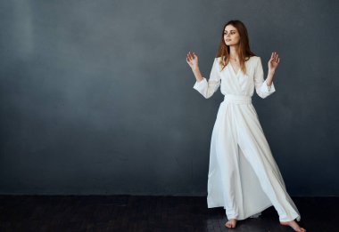 Güzel kadın beyaz elbise stüdyosu dans gri arka plan modeli yapıyor.