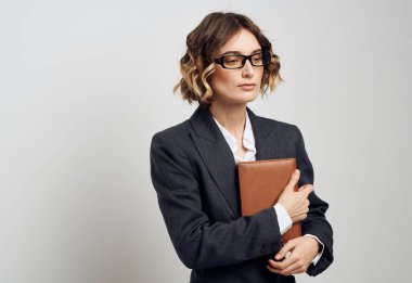 Klasik takım elbiseli bir iş kadını, elinde bir kitapla evin içinde hafif bir arka plan tutuyor.