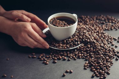 Gri bir masada aromatik kahve çekirdekleri ve bir bardağın yanında da bir bardak su.