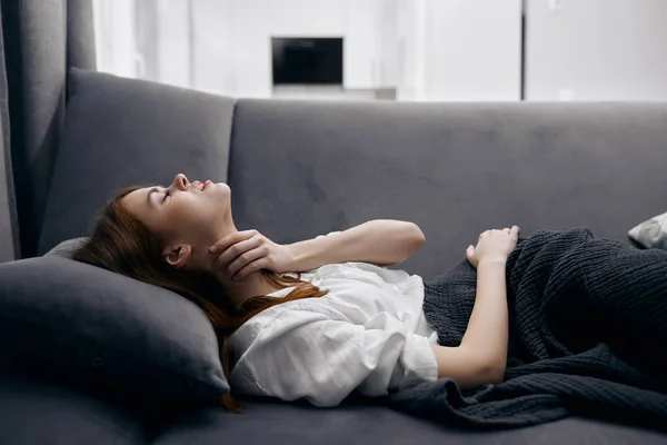 Una mujer se acuesta en el sofá cubierta con una manta sensación de malestar enfermedad —  Fotos de Stock