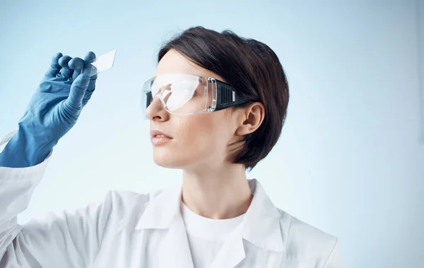 Assistente de laboratório feminino em luvas médicas olhando para o vidro de um microscópio — Fotografia de Stock