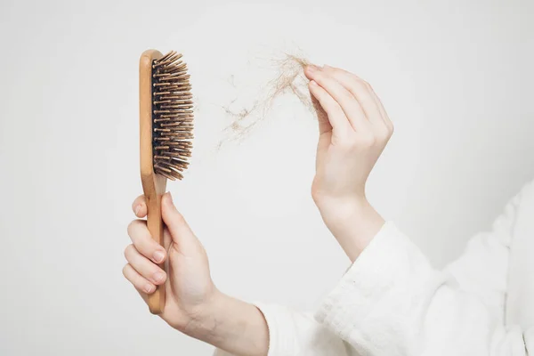 woman removes a bun of hair with a wooden comb on a light background health problems loss