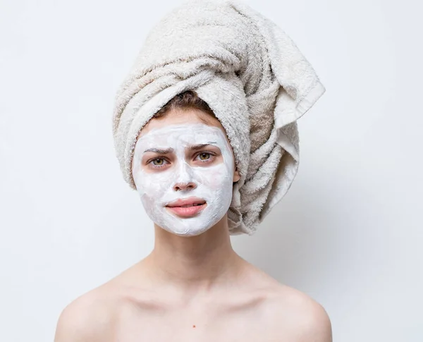 Femme nue avec de la crème blanche sur le visage et une serviette sur la tête — Photo
