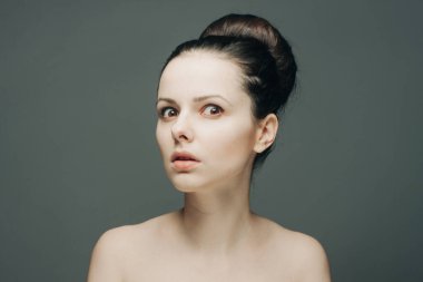 Çekici esmer, çıplak omuzlu, açık tenli, gri arka planlı.