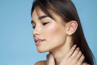 Güzel esmer, çıplak omuzlar uzun saç bakımı mavi arka plan