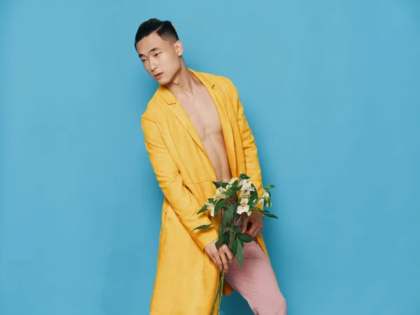 Homem asiático em um fundo azul com um buquê de flores dobradas para o lado — Fotografia de Stock