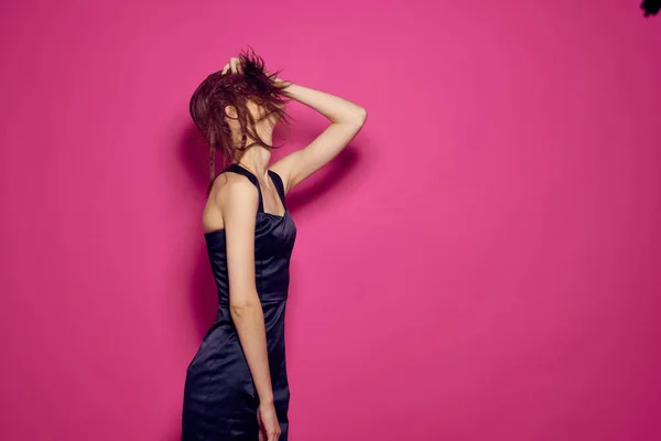 Una mujer en un vestido oscuro toca el pelo de su cabeza con su mano sobre un fondo rosa —  Fotos de Stock