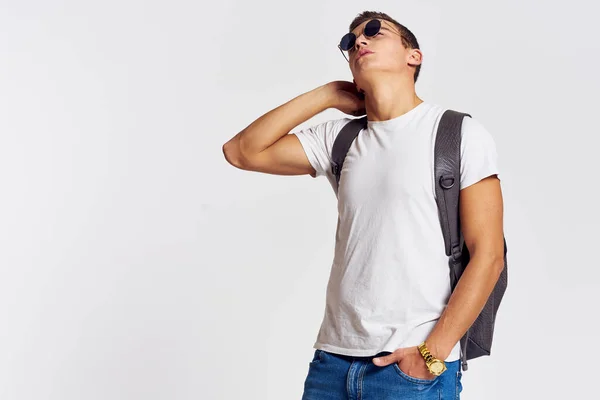 Man in zonnebril met een rugzak op zijn rug en in een wit t-shirt op een lichte achtergrond bijgesneden weergave van emotie — Stockfoto