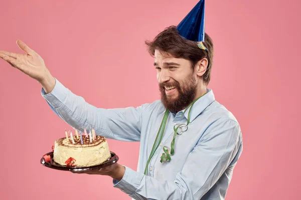 Een man in een shirt met een taart in zijn handen en een feestelijke pet op zijn hoofd — Stockfoto