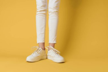 Kadın ayaklı beyaz spor ayakkabılar. Çekici, moda sarısı arka plan.