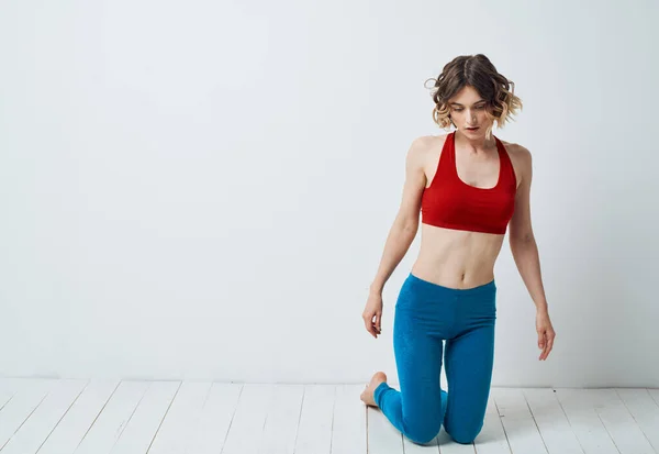 Nő gyakorolja jóga egy világos szobában és kék Leggings piros póló — Stock Fotó
