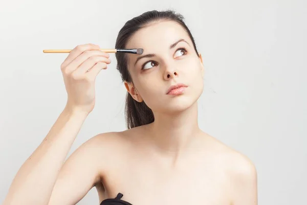 Woman with bare shoulders applying makeup brush on face procedure — Stock Photo, Image