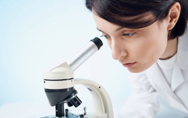 Doktor kadın doktor, doktor önlüğü ve eldivenleriyle mikroskop altında kapalı bir masaya bakıyor.