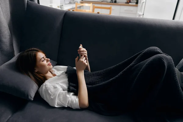 Mulher descansando no sofá com um telefone na mão e uma xadrez cinza em suas pernas — Fotografia de Stock