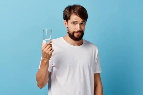 Homem com barba segurando vidro de água na mão sobre fundo azul branco t-shirt modelo recortado vista — Fotografia de Stock