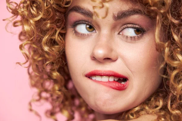 Mulher Curly cabelo grimace morde o lábio com um olhar para o fundo rosa — Fotografia de Stock