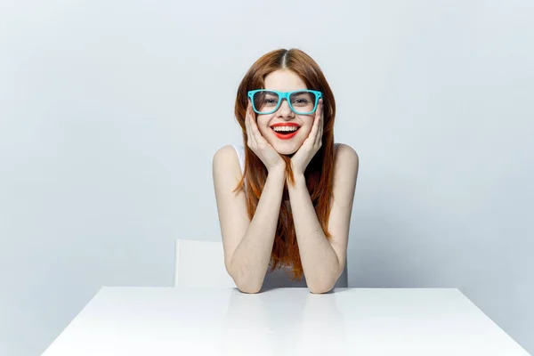Bonita mujer pelirroja sentada en la mesa con gafas azules labios rojos emociones glamour — Foto de Stock