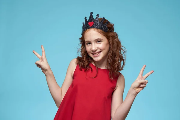 Mädchen mit lockigem Haar mit Krone auf dem Kopf rotes Kleid Lebensstil blauer Hintergrund — Stockfoto