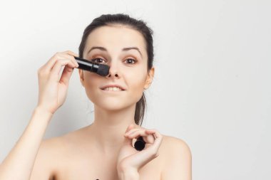 Çekici esmer, yüzünde krem, ellerinde fırça, makyaj yapıyor.