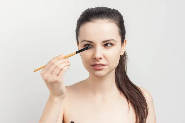 Cute bare-shouldered brunette applying makeup on face cropped view — Stock Photo, Image