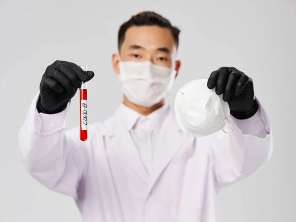 En man med asiatiskt utseende i svarta handskar håller en skyddande mask i händerna ett blodprov — Stockfoto