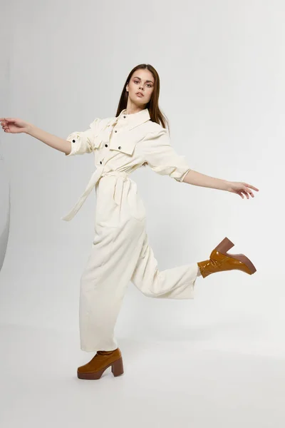 Модная женщина в белом комбинезоне бежит в сторону в сапогах и жестах руками — стоковое фото
