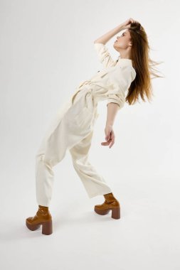 Beyaz tulumlu şık bir kadın saçını tutarak arkasını yasladı.