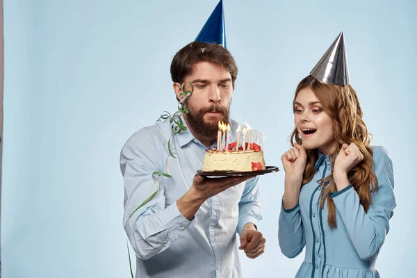 Hombre y mujer celebran cumpleaños con pastel y en sombreros sobre fondo azul — Foto de Stock