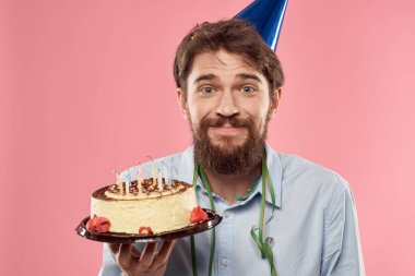 Ellerinde pasta ve kafasında şenlik şapkası olan tişörtlü bir adam.