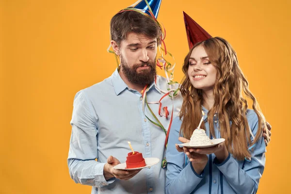 Enerjik bir adam ve doğum günü pastalı güzel bir kadın sarı arka plan disko partisinde şapkalı. — Stok fotoğraf
