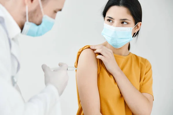 Egy fehér köpenyes hivatásos orvos oltást ad be egy orvosi maszk védőoltással rendelkező nő vállába — Stock Fotó