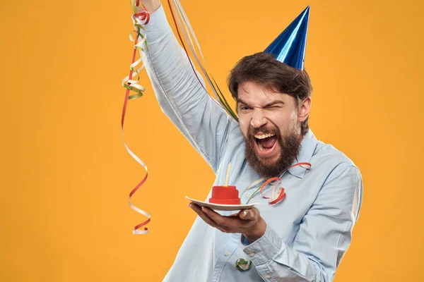 Homme joyeux avec un gâteau sur un fond jaune casquette de vacances d'anniversaire sur sa tête — Photo