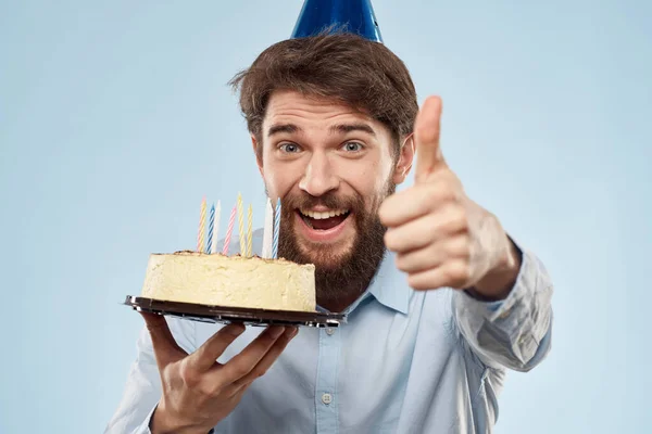 Pastel en un plato y hombre de cumpleaños con una gorra en su cabeza fondo azul — Foto de Stock