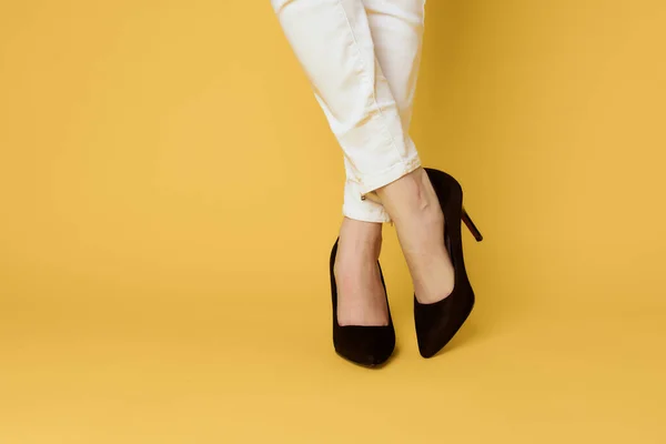 Γυναικεία πόδια μαύρα παπούτσια μόδας ελκυστική εμφάνιση λευκό τζιν κίτρινο φόντο — Φωτογραφία Αρχείου