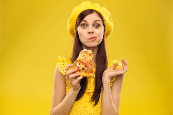 Mujer en sombrero amarillo con un pedazo de pizza en las manos sobre un fondo amarillo recortado vista de modelo de emoción — Foto de Stock