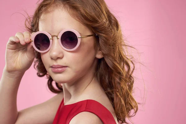 Mädchen mit lockigem Haar dunkle runde Brille Spaß rotes Kleid rosa Hintergrund — Stockfoto