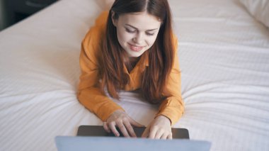 Yatak odasındaki kadın dizüstü bilgisayarlı iletişim teknolojisiyle yatakta uzanıyor.