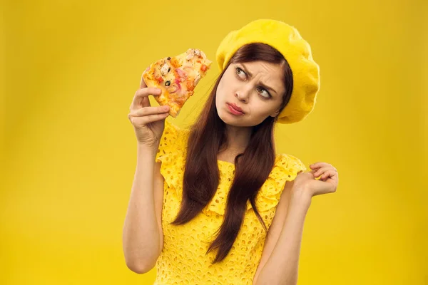 Mulher de chapéu amarelo com um pedaço de pizza em suas mãos em um fundo amarelo corte vista de modelo de emoção — Fotografia de Stock