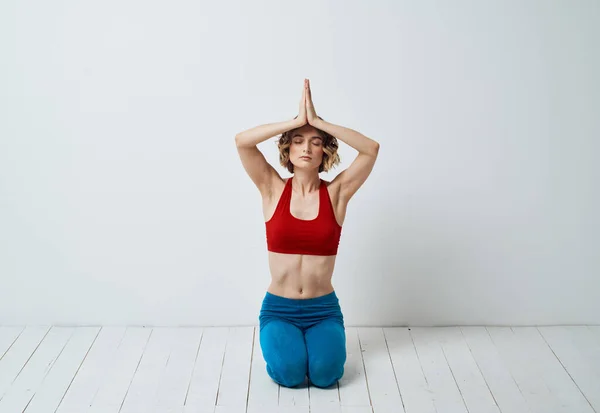 En kvinna sitter på ett ljust golv inomhus med händerna förenade med yoga asanas för avkoppling — Stockfoto
