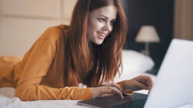 Yatakta dizüstü bilgisayarla internetten sohbet eden neşeli, güzel bir kadın.