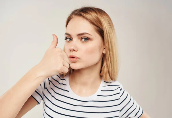 Allegro bionda su uno sfondo chiaro mostra un dito e un ritagliato a strisce T-shirt può essere visto — Foto Stock