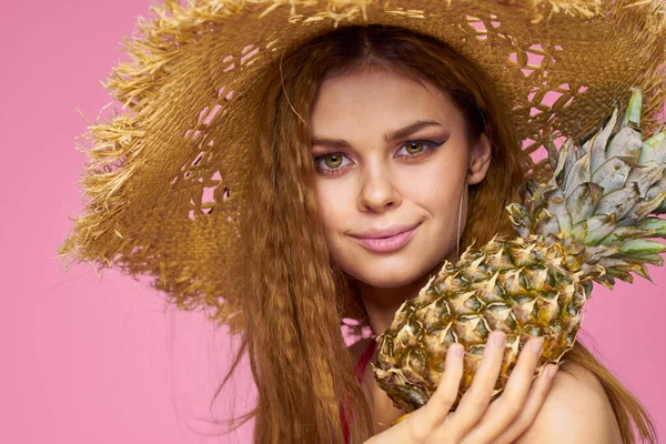 Woman with a gun in hands of a straw hat bright makeup exotic fruits summer pink background