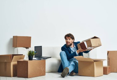 Bir adam kutunun zemininde oturuyor ve ofis eşyaları bavulunu boşaltıyor.