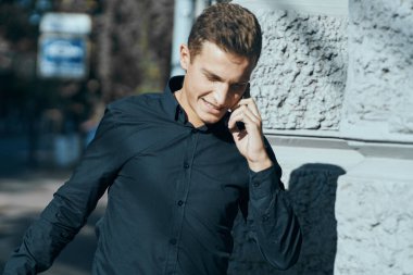 Siyah gömlekli bir iş adamı sokakta telefonla konuşuyor.