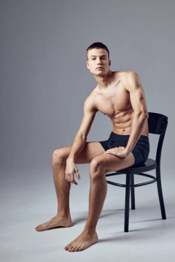 Şişirilmiş kaslı vücudu olan sportif bir adam sandalyeye oturmuş izole edilmiş arka plan fitness