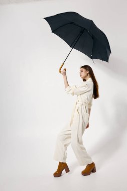 Kafasında açık şemsiyeyle şık bir kadın. Yağmurdan korunuyor. Kahverengi çizmelerden modern tarzda.