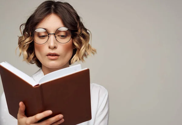 Vrouw met een notitieblok in haar handen en het dragen van een bril op een grijze achtergrond bijgesneden weergave van een licht shirt — Stockfoto