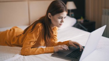 Kadın dizüstü bilgisayarın önünde yatağa uzanıyor. Serbest iş interneti.